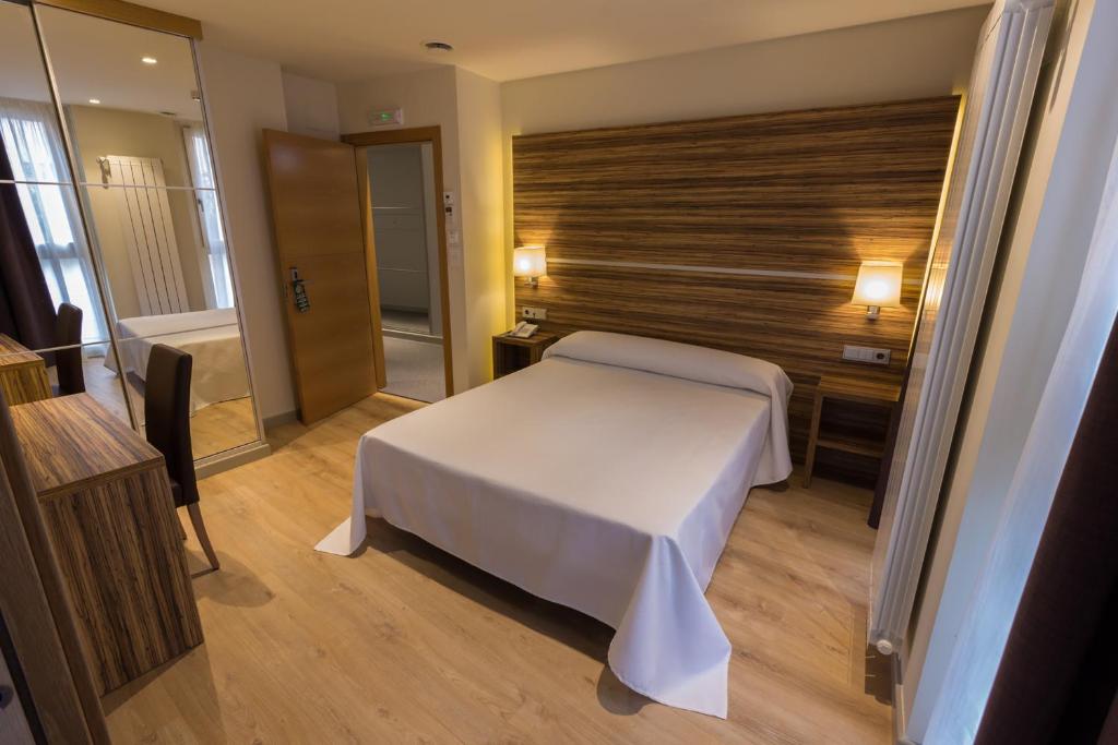 um quarto com uma cama branca e piso em madeira em Hotel Novo Cándido em Ourense