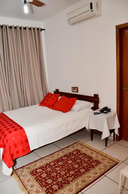a bedroom with a bed with red pillows and a rug at Pousada Victor in Ribeirão Claro