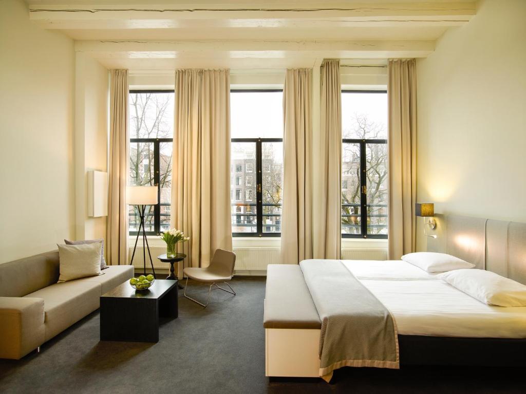 Hapimag Apartments Amsterdam في أمستردام: غرفة نوم بسرير واريكة ونوافذ