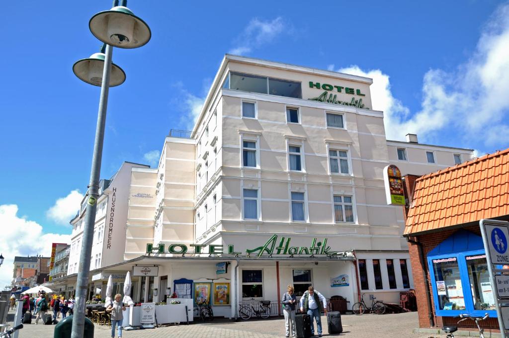 a white building on a street with people standing outside at Hotel Atlantik in Borkum
