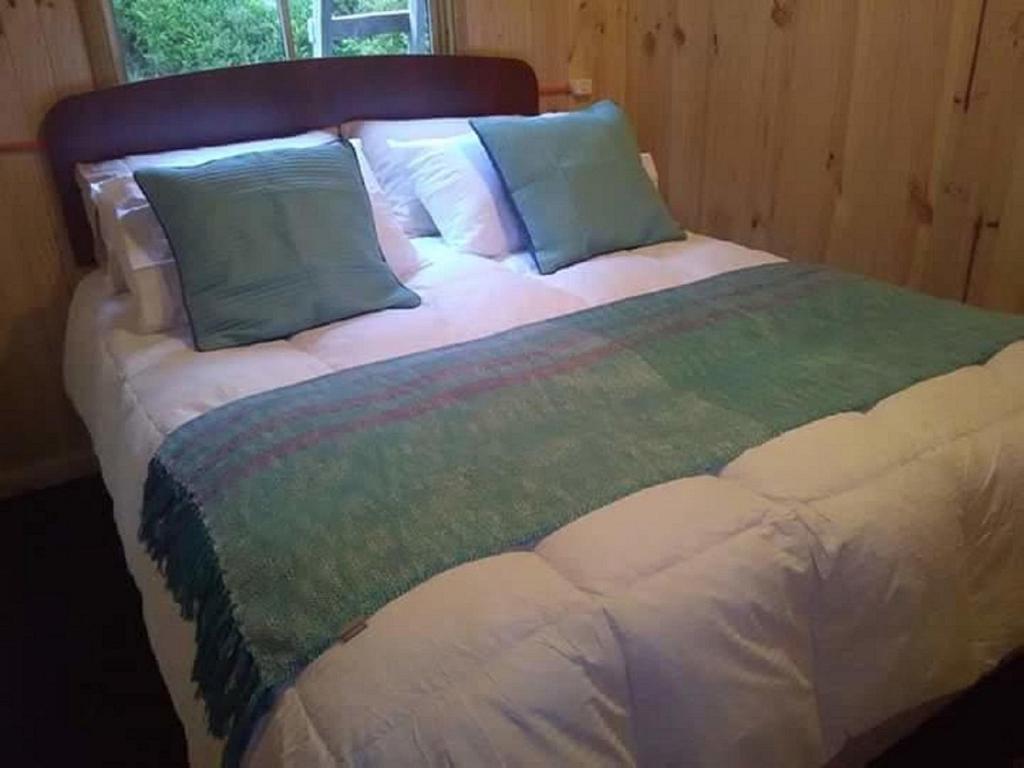 Una cama grande con almohadas azules y verdes. en Cabaña La Sierra de Cochamó, en Cochamó