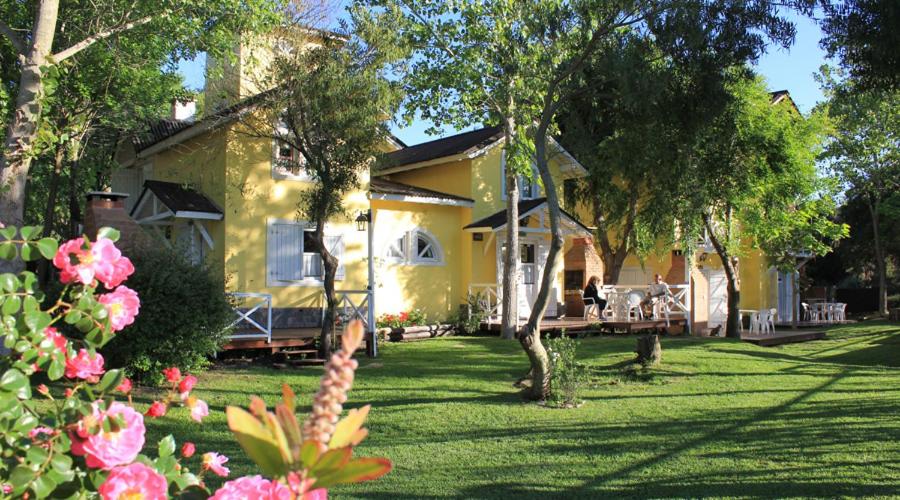 una casa amarilla con un patio con flores y árboles en Cabañas Mi Lugar en Las Gaviotas
