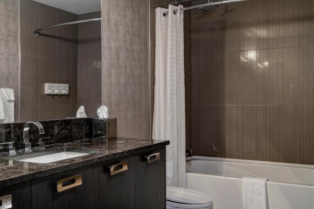 a bathroom with a sink and a tub and a toilet at Hotel Arts Kensington in Calgary