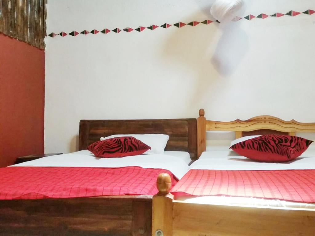 two beds with red pillows in a room at Maasai Simba Camp in Amboseli