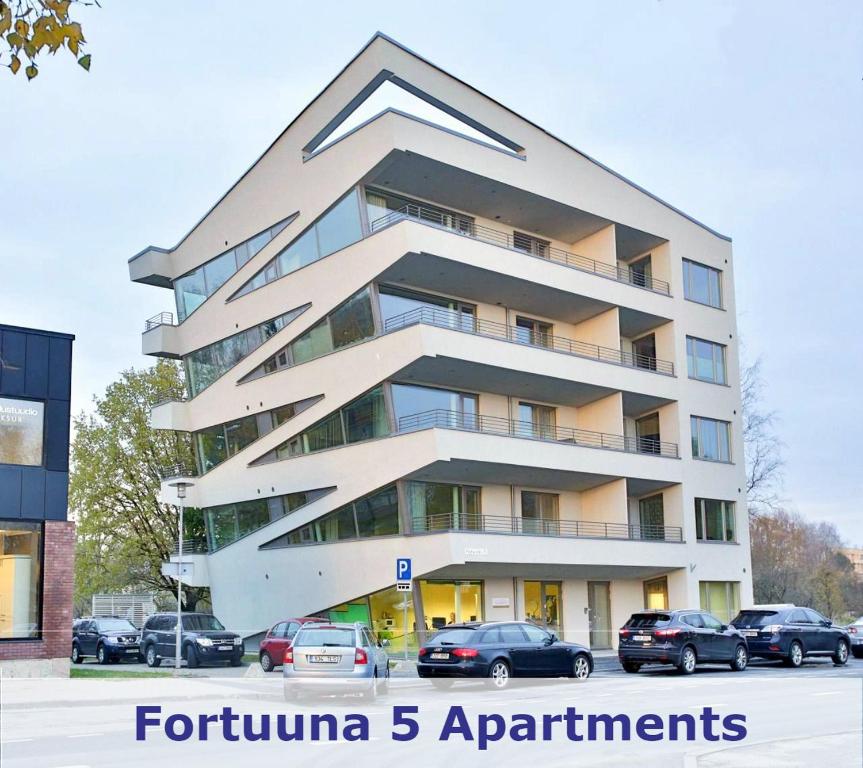 a tall white building with cars parked in a parking lot at Fortuuna 5 Apartment in Tartu