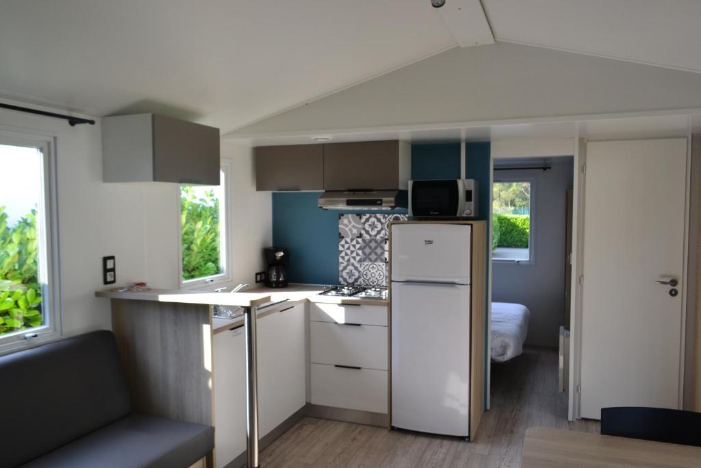 a small kitchen with a white refrigerator and a bed at Village Océanique in Le Bois-Plage-en-Ré
