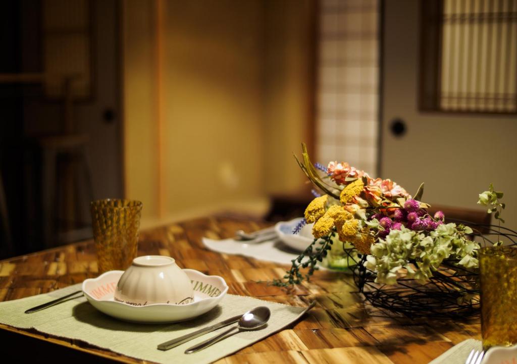 einem Holztisch mit Tellern, einer Teekanne und Blumen in der Unterkunft 今日都 Kyoto Guesthouse in Kyoto