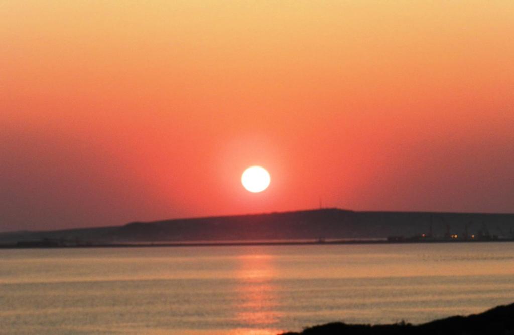 a sunset over the water with the sun on a hill at Langebaan Paradise Beach self catering in Langebaan