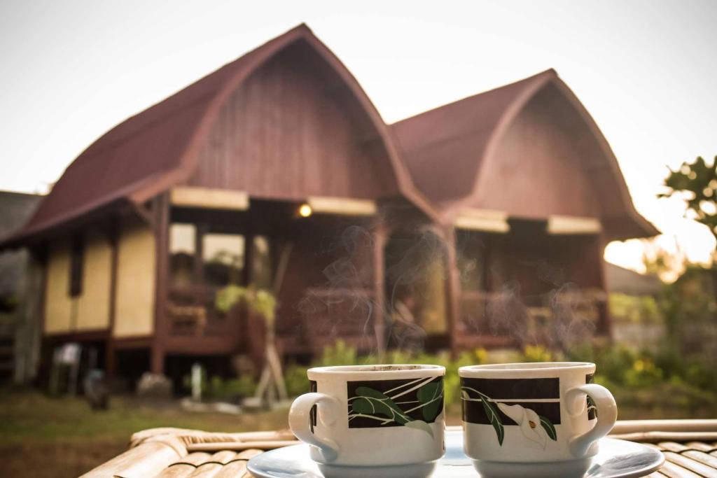 two coffee cups sitting on a table in front of a house at Lia Jaya Bungalows in Gili Meno