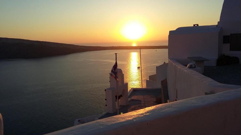 a sunset over the water with a flag on a building at Fotinos Houses in Oia