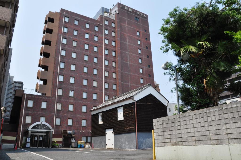 um grande edifício de tijolos com uma pequena casa em frente em Kawagoe Daiichi Hotel em Kawagoe