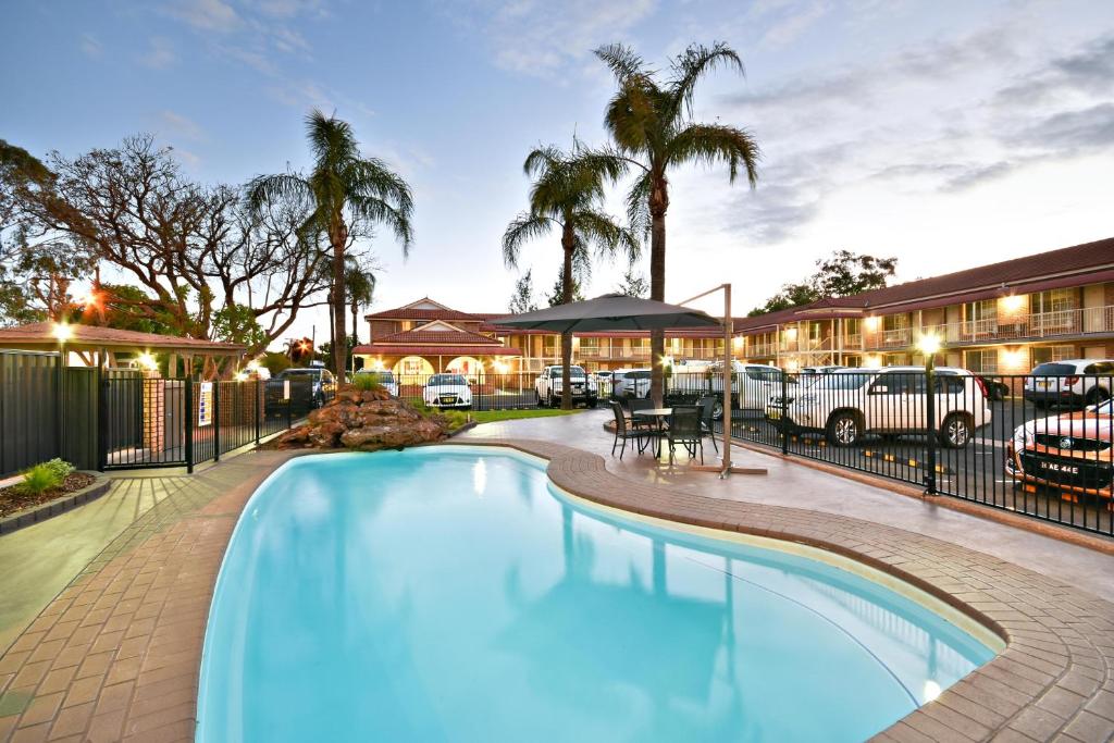 a pool in front of a hotel with palm trees at The Aberdeen Motel in Dubbo