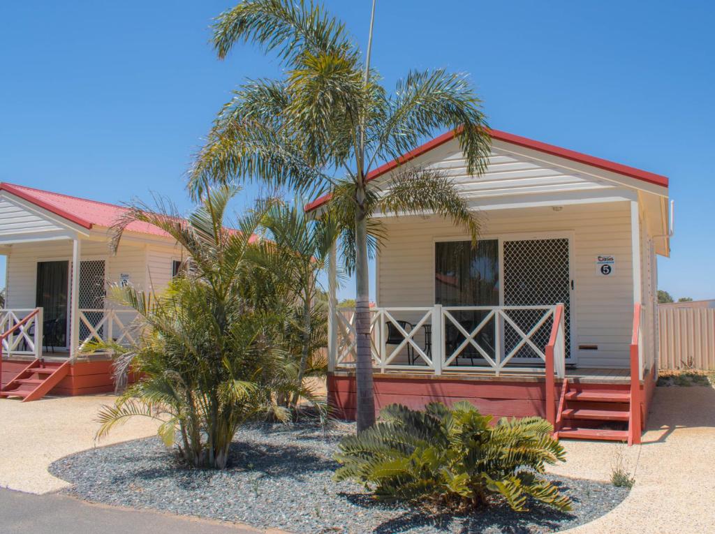 a house with palm trees in front of it at Outback Oasis Caravan Park in Carnarvon