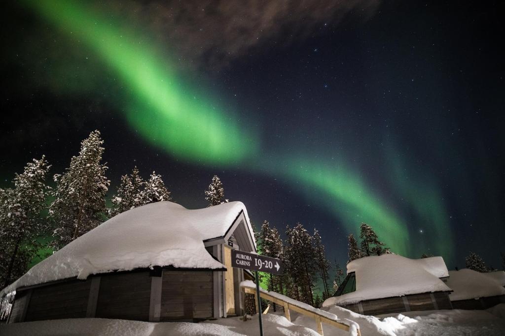 an aurora over a ski lodge in the snow at Northern Lights Village in Saariselka