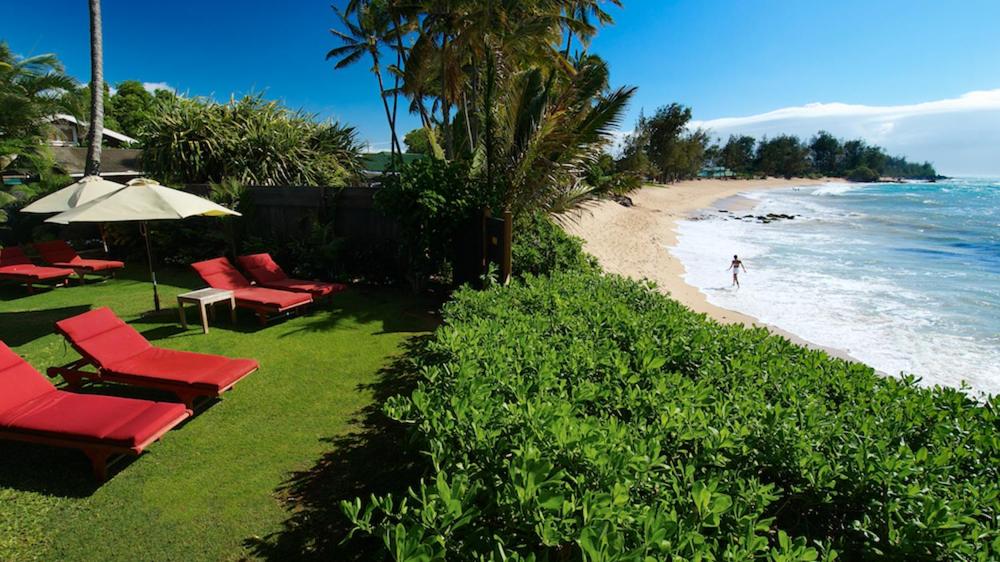 a beach with red chairs and an umbrella and the ocean at Paia Inn in Paia