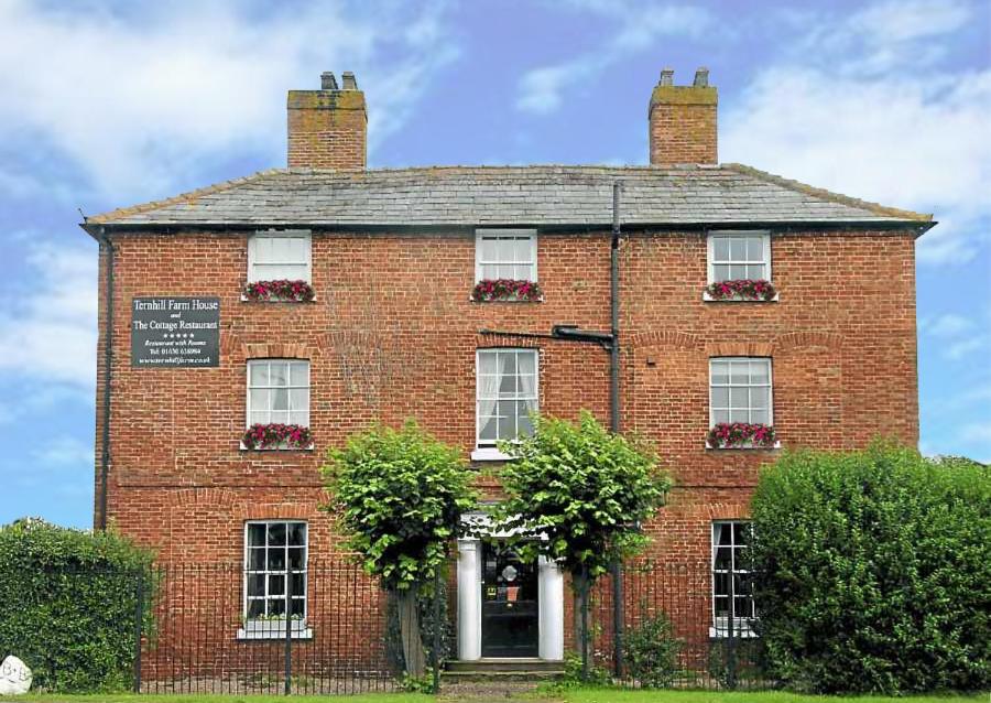 um grande edifício de tijolos vermelhos com arbustos à frente em Ternhill Farm House - 5 Star Guest Accommodation with optional award winning breakfast em Market Drayton