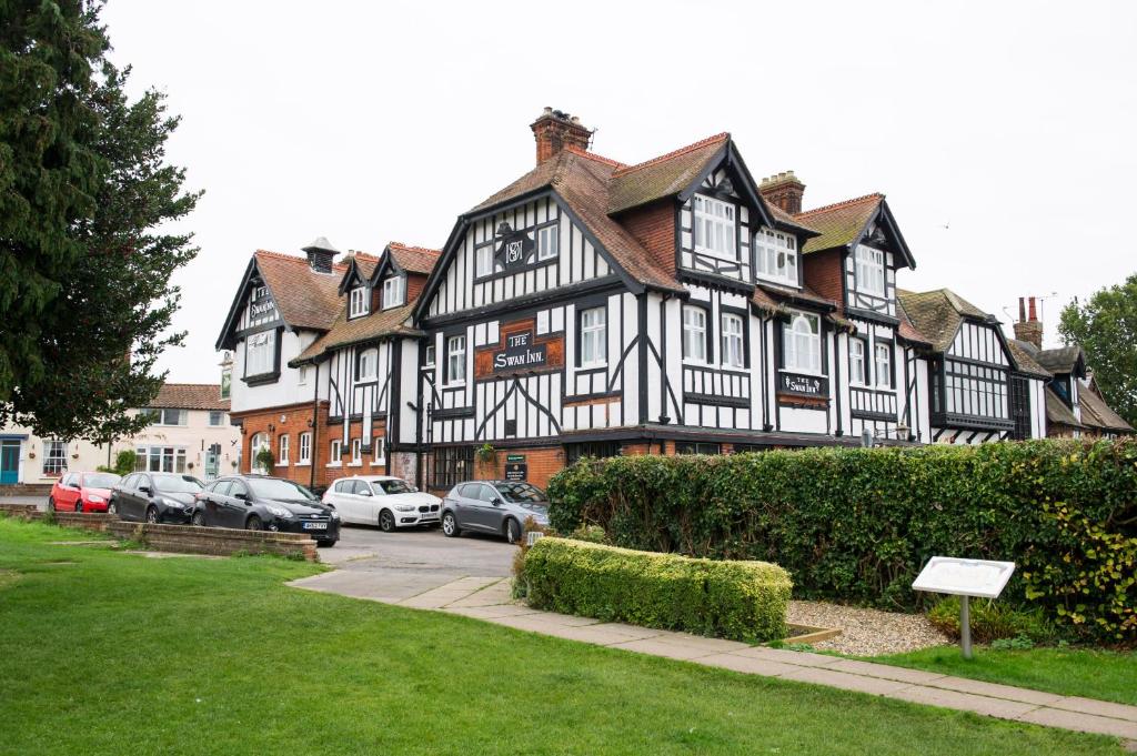 un gran edificio blanco y negro con coches aparcados delante en The Swan Inn by Innkeeper's Collection en Horning