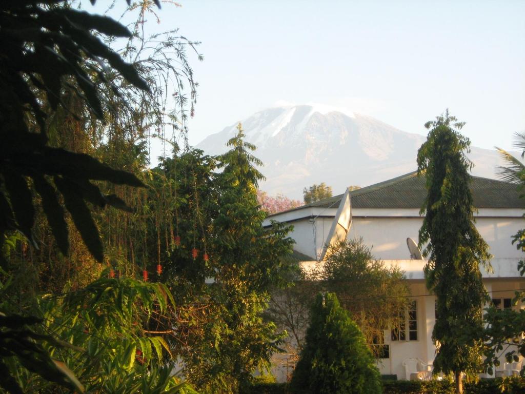 a mountain in the distance behind a building with trees at Kitolie Home and Lodge in Moshi