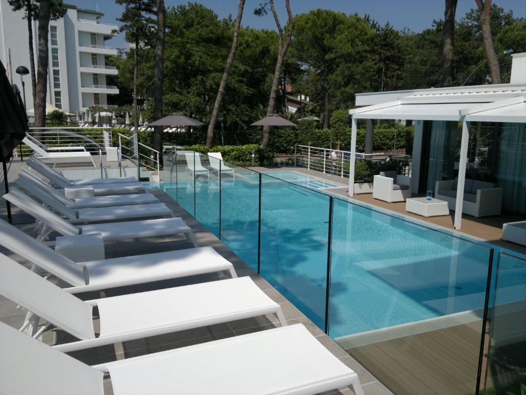 a swimming pool with white lounge chairs next to a building at Suite Erica Lignano Hotel in Lignano Sabbiadoro