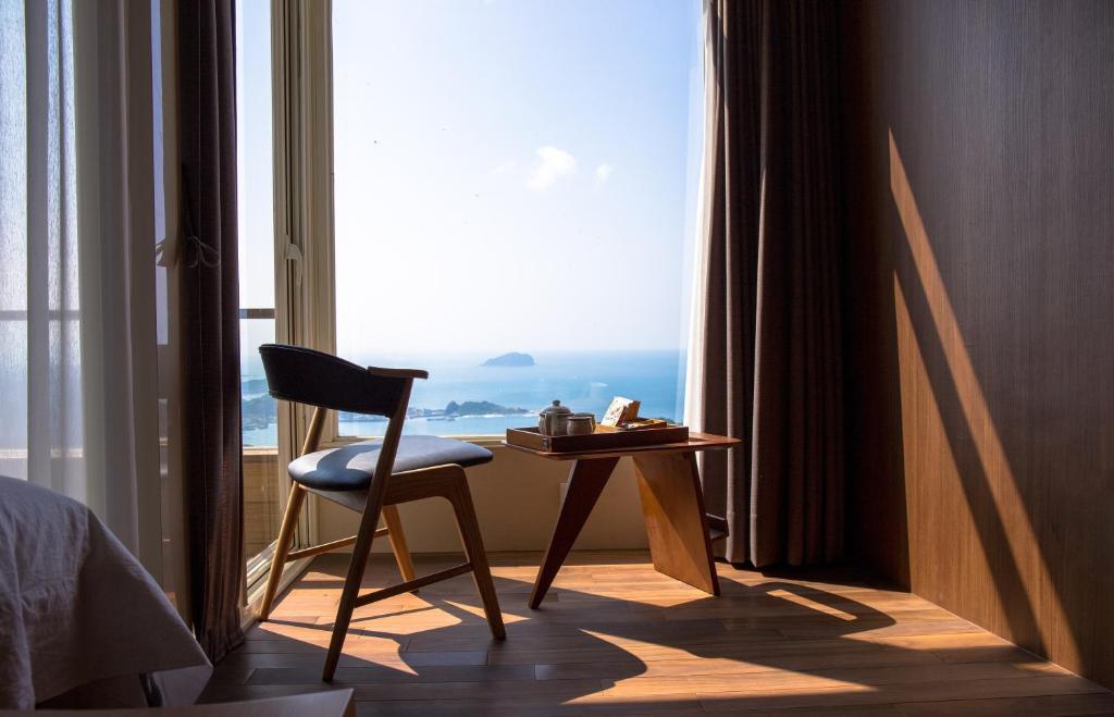 a room with a chair and a table in front of a window at Something Easy Inn in Jiufen