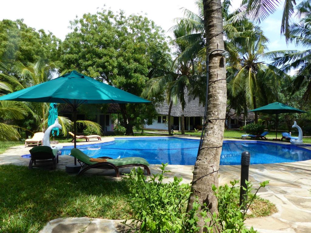 a swimming pool with chairs and an umbrella at Residence Maison M&uuml;ge in Kilifi