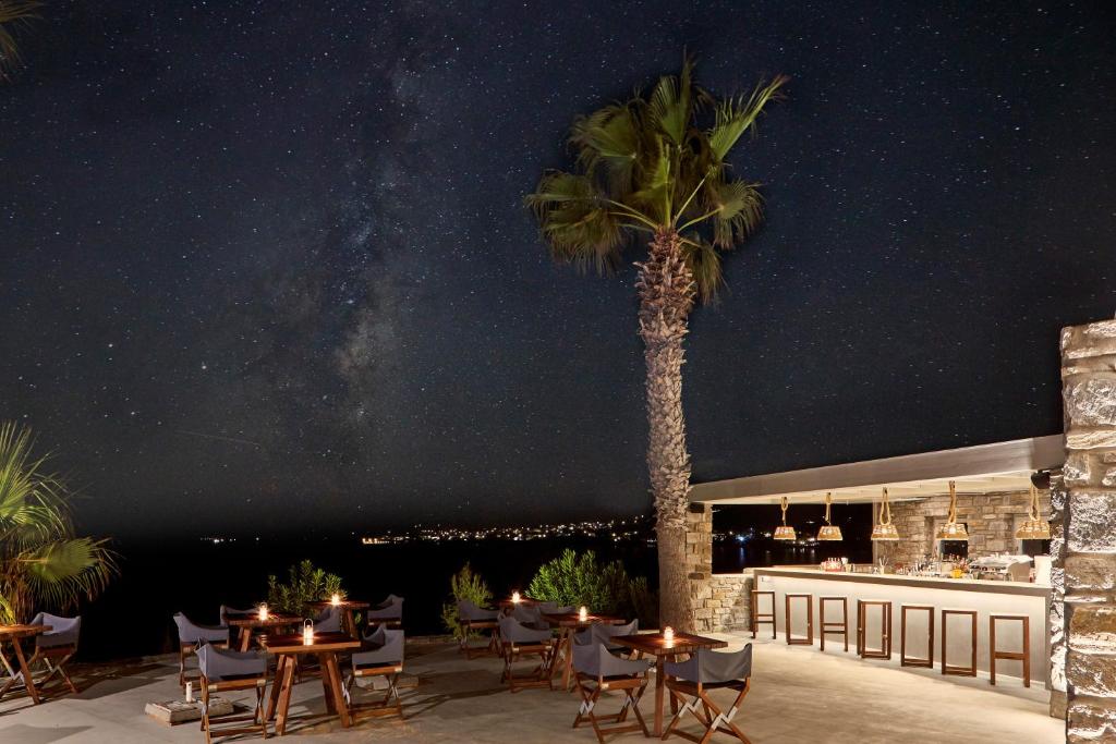 a palm tree on a patio with tables and chairs at Poseidon of Paros Hotel & Spa in Chrissi Akti