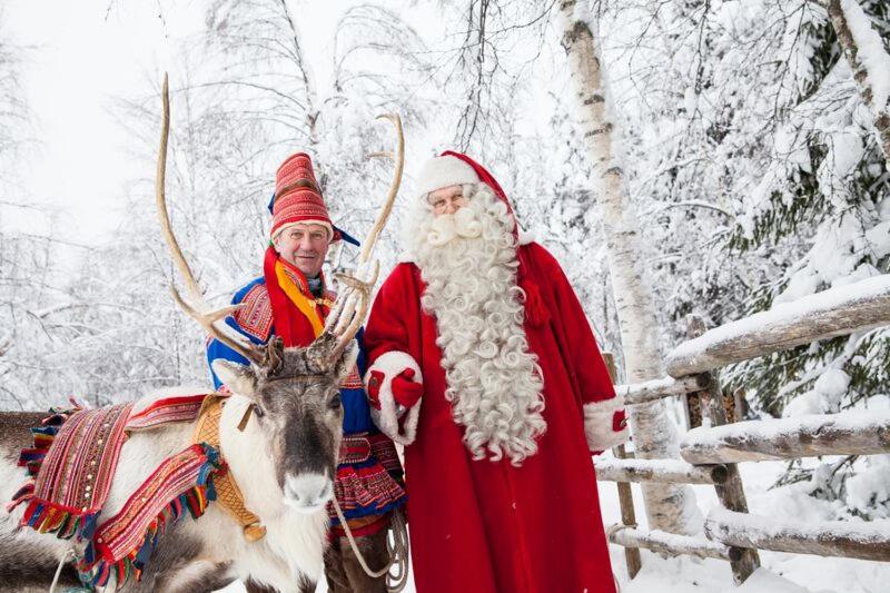 Dois homens vestidos de Pai Natal ao lado de uma rena. em RovaVisit Apartments Paroni em Rovaniemi