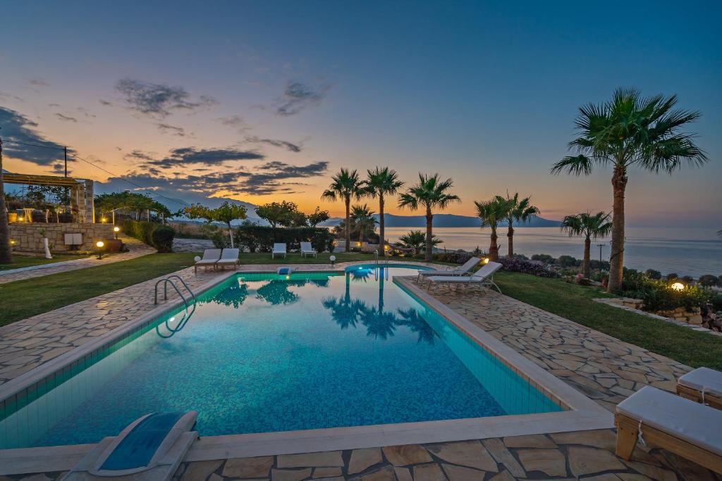 a swimming pool with palm trees and the ocean at Aneria Suites in Episkopi