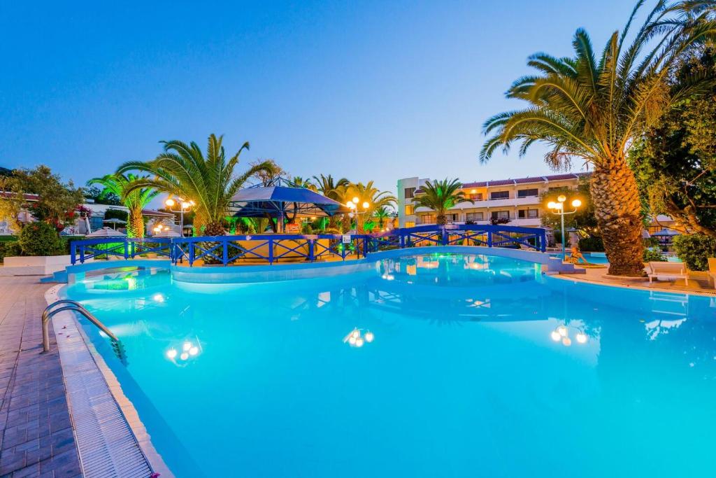 a pool at night with palm trees and buildings at Filerimos Village Hotel in Ialysos