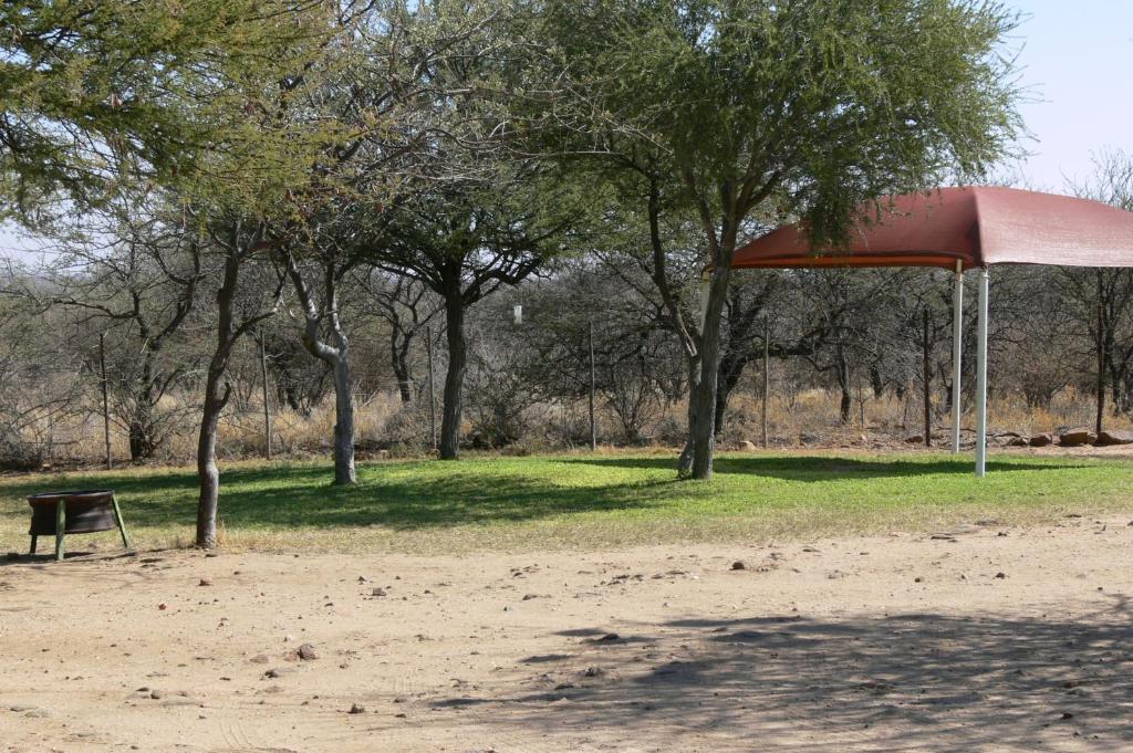 a red umbrella in a park with trees at Ombo Rest Camp in Okahandja