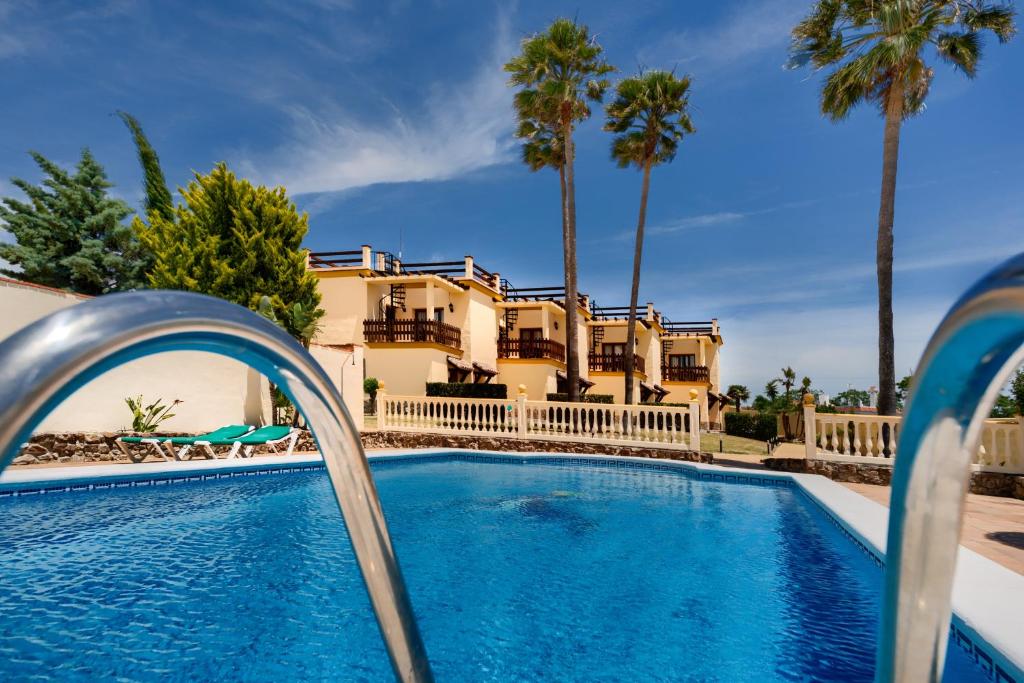 a pool in front of a house with palm trees at Apartamentos Villafaro Conil in Conil de la Frontera