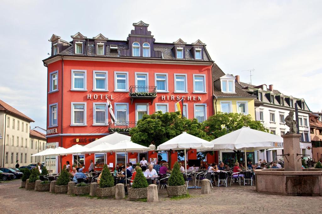 um edifício vermelho com pessoas sentadas em mesas à frente dele em Hotel Hirschen em Constança
