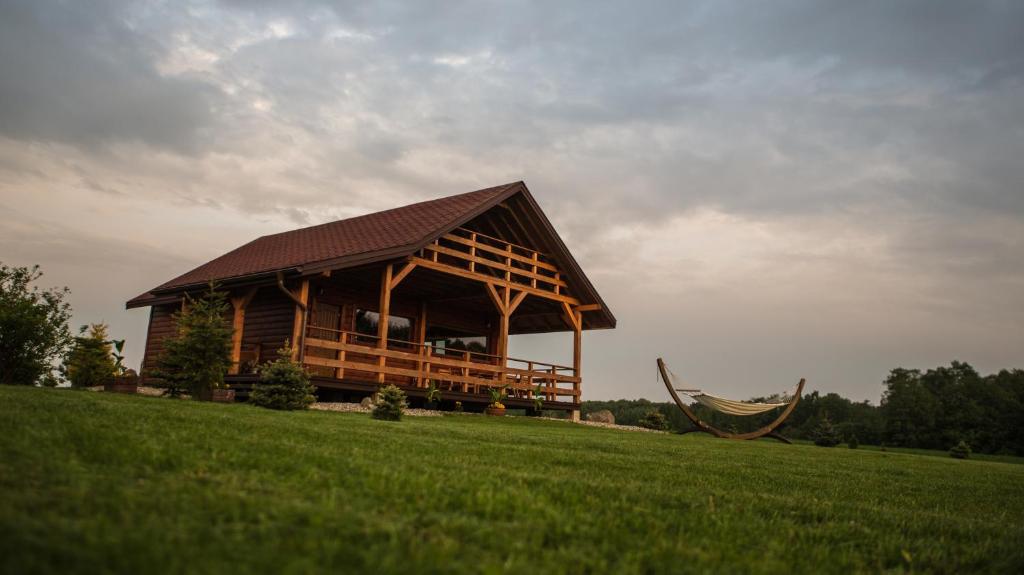 a large wooden cabin on a grassy hill with a hammock at Domki nad Jeziorem in Rajgród