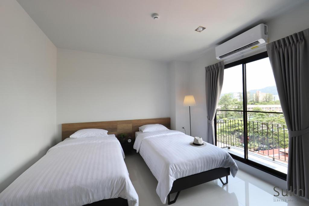 two beds in a room with a large window at Sukh Serviced Apartment in Ban Kohong