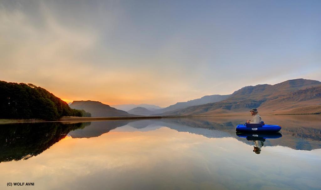 Um homem está sentado num barco num lago. em Giantscup Wilderness Reserve em Underberg