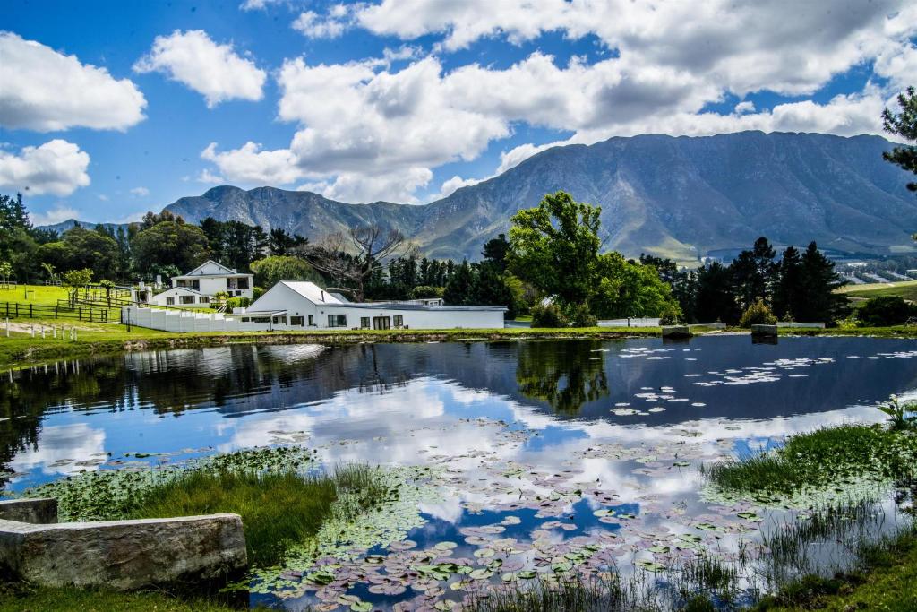 a lake with a house and mountains in the background at High Season Farm Luxury Cottages in Hermanus