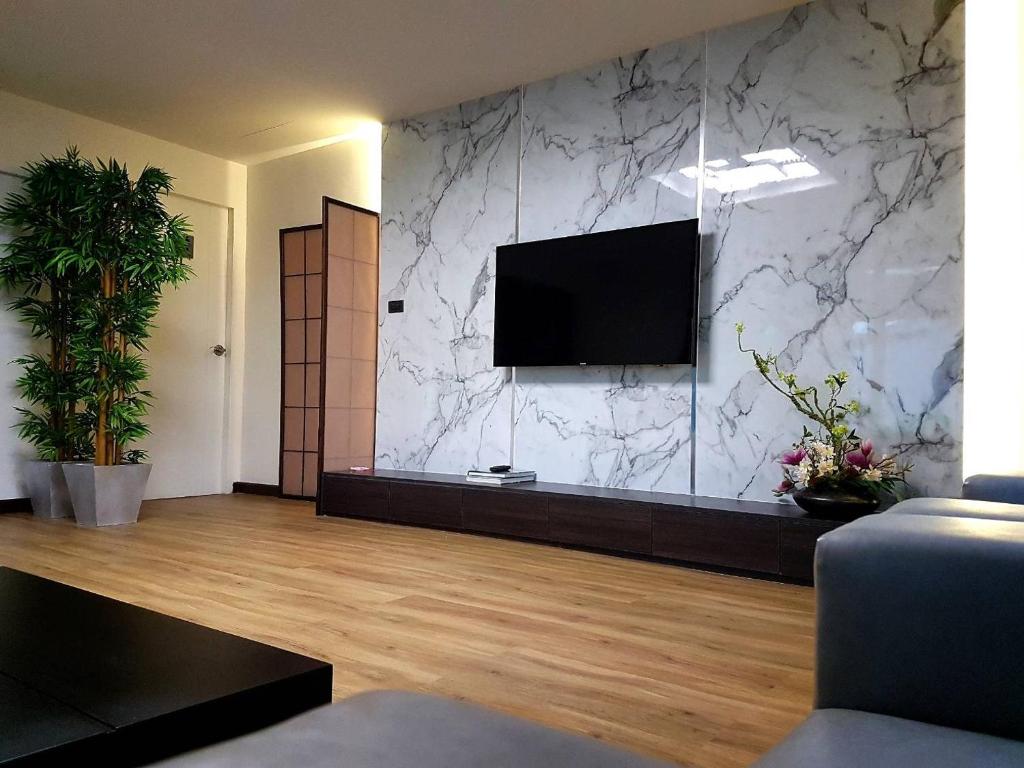 A furnished lounge facing a marble-pattern TV wall and large potted plant.