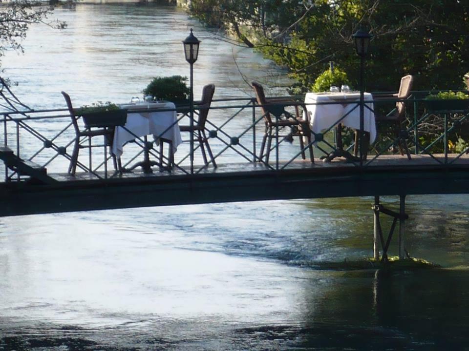 une table et des chaises sur un pont sur une rivière dans l'établissement Les Terrasses de David et Louisa, à LʼIsle-sur-la-Sorgue