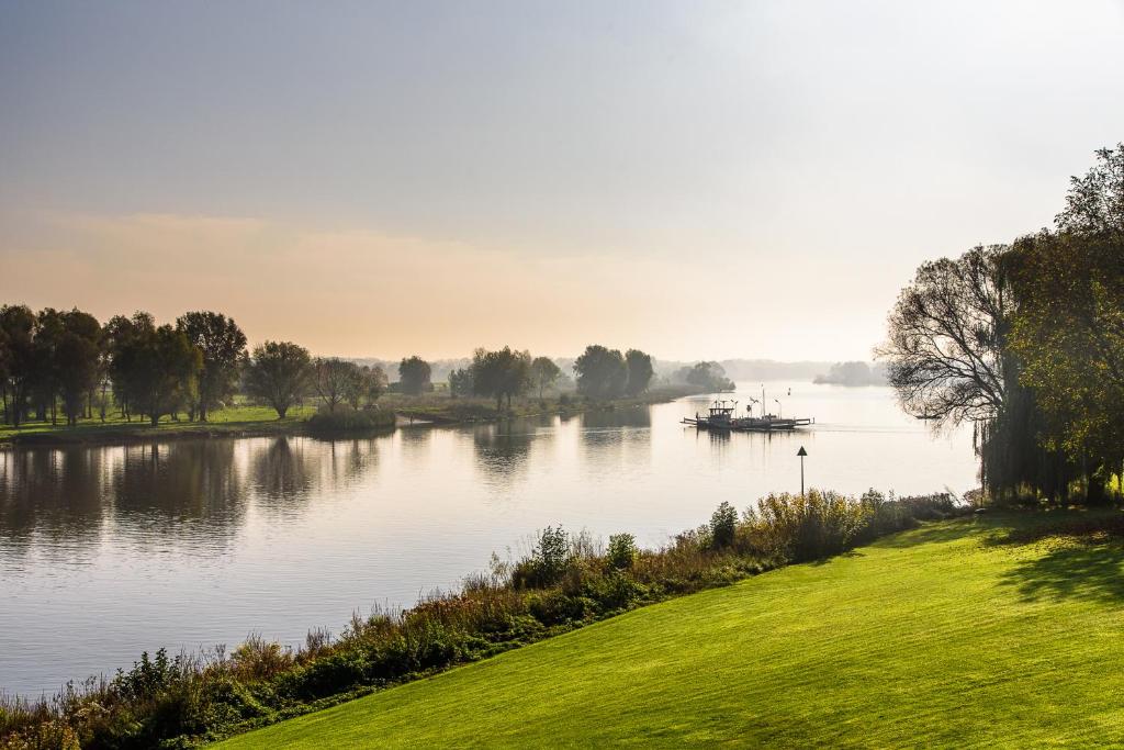 een boot op een rivier met bomen en een veld bij Vakantie aan de Maas in Broekhuizen