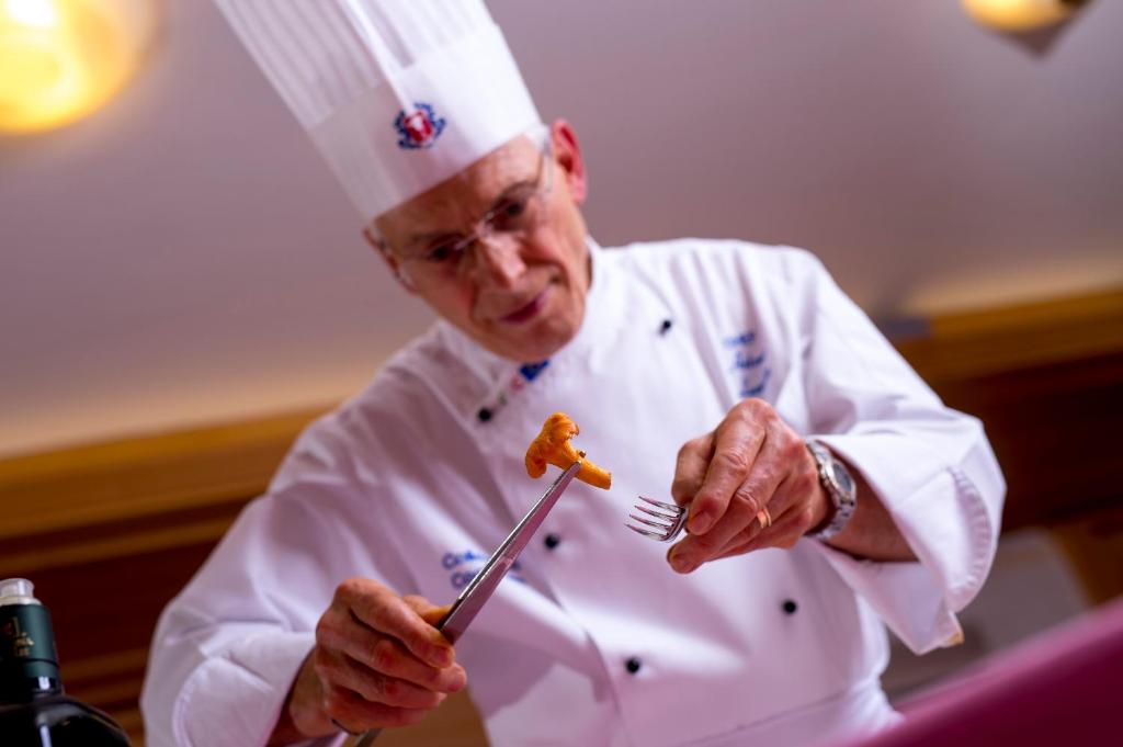 uno chef che tiene in mano una forchetta e un pezzo di cibo di Hotel Villa Rosella Park & Wellness a Canazei