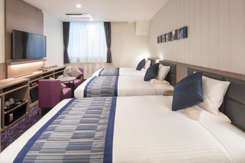 a hotel room with three beds and a flat screen tv at Hotel Mystays Gotanda Station in Tokyo