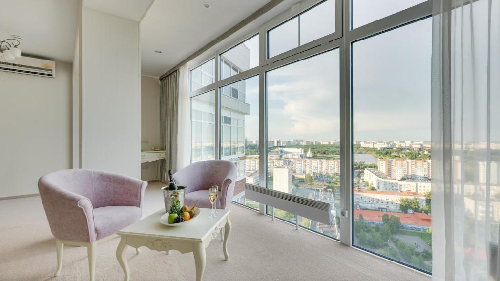 a living room with two chairs and a table and large windows at Gala Hotel in Surgut