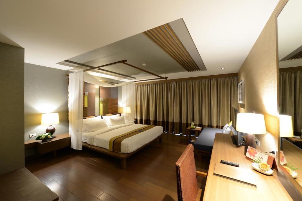 A warmly lit room with a large bed, desk, and full-height curtained window.