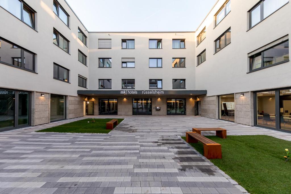 a large white building with benches in the courtyard at mk | hotel rüsselsheim in Rüsselsheim
