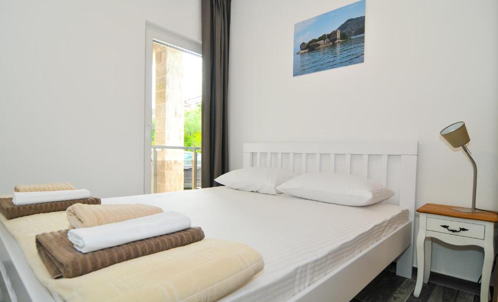 a white bedroom with a bed and a chair at Apartments Edera in Tivat