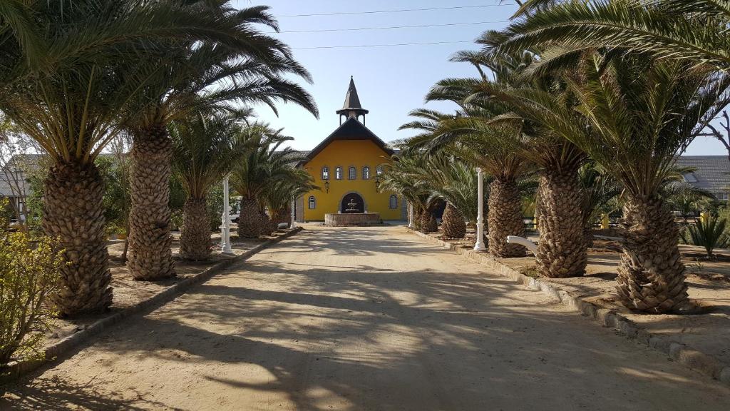 eine Reihe von Palmen vor einem gelben Gebäude in der Unterkunft Gut Richthofen in Swakopmund