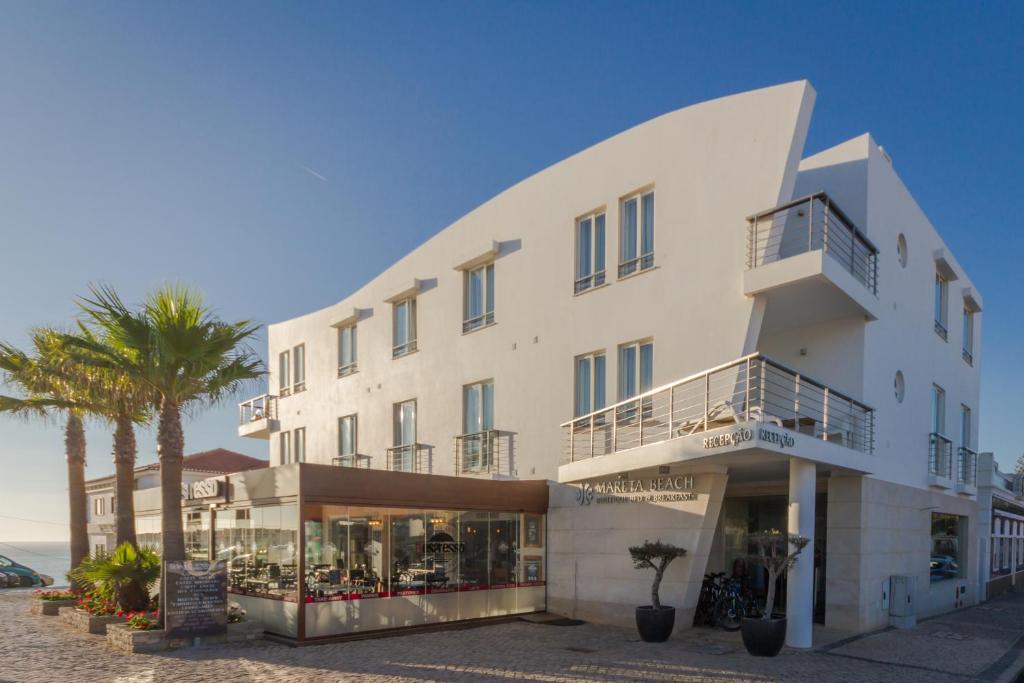 a large white building with a palm tree in front of it at Mareta Beach - Boutique Bed & Breakfast in Sagres