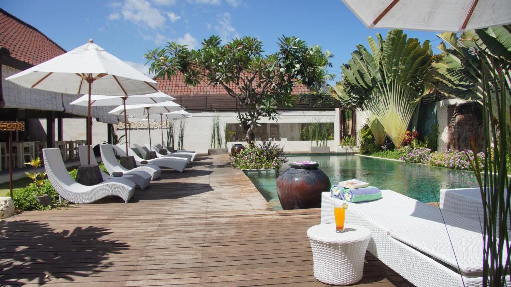 una piscina con sedie a sdraio e ombrelloni bianchi di Katala Suites and Villas a Sanur