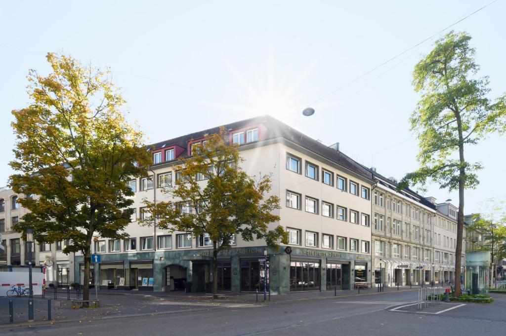 a large white building on a street with trees at Hotel City Zürich Design & Lifestyle in Zurich