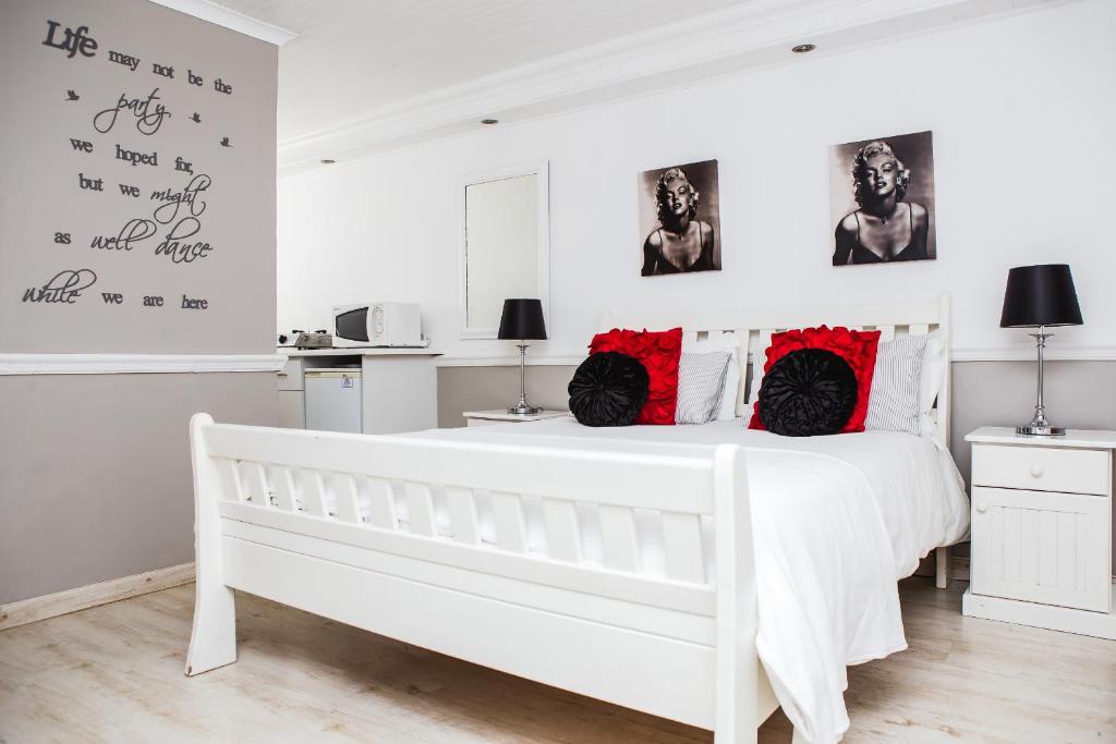 a white bedroom with a white bed with red pillows at Golden Key Guesthouse in Vredenburg